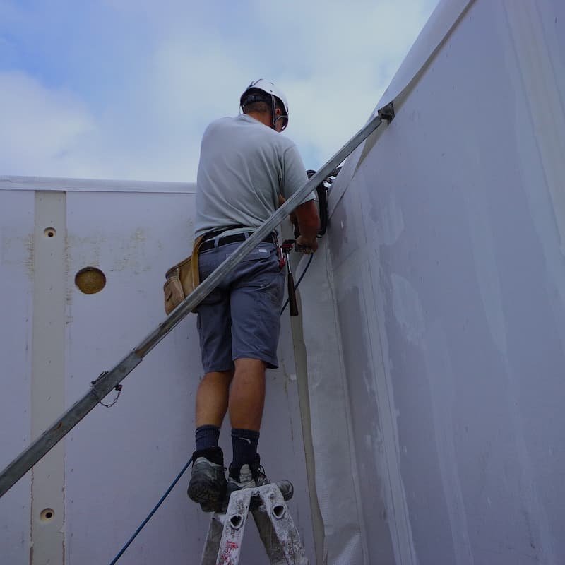 Operaio specializzato in sicurezza su scala, applica pannello isolante per garantire la qualità del lavoro edilizio.