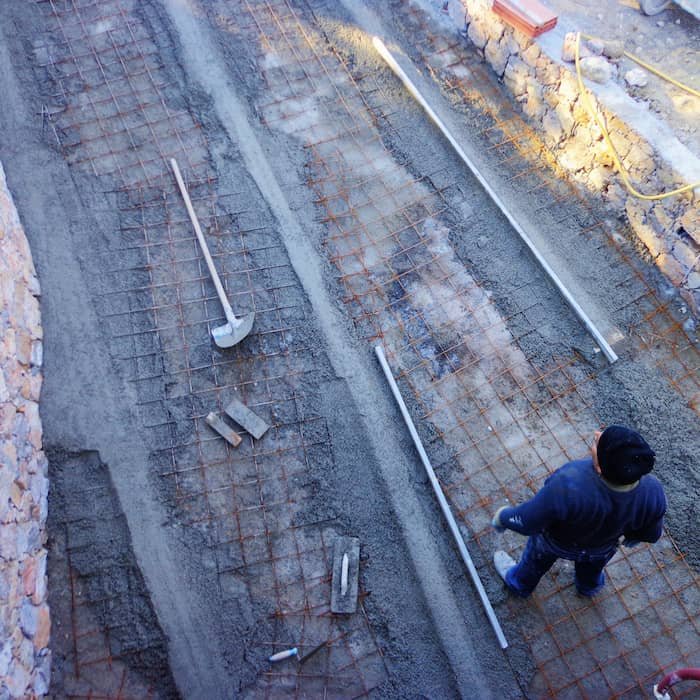 Operaio edile prepara il fondo per la pavimentazione con rete elettrosaldata e guide di livello durante una ristrutturazione strutturale.